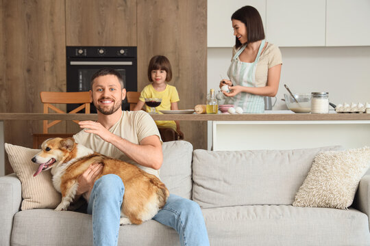 Young man with Corgi dog on sofa and his family making pancakes in kitchen - Powered by Adobe