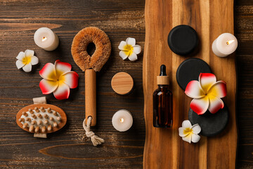 Beautiful spa composition with stones, candles, massage body brushes and plumeria flowers on brown wooden background