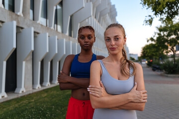 Two fit women posing with crossed arms in front of modern building