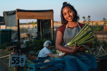 Young farmer woman holding fresh leeks in community garden