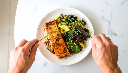 Healthy meal of salmon, quinoa, and greens. Hands holding fork and knife over a plate