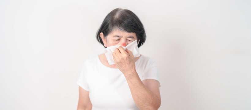 Elderly woman blowing her nose with tissue for concepts of Common Cold, Influenza, Flu, Hay, Fever, Covid 19, Respiratory Infection, Sinusitis, Allergic Rhinitis, Allergy, Medical and health care