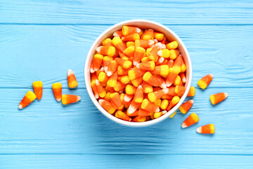 Bowl of tasty Halloween candy corns on blue wooden background