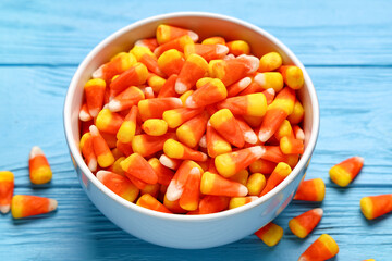 Bowl of tasty Halloween candy corns on blue wooden background