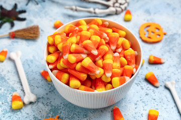 Bowl of tasty candy corns with Halloween decorations on blue grunge background