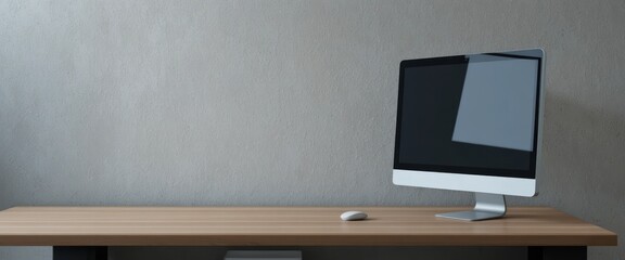 Modern desktop computer monitor and white mouse on a wooden desk against a textured gray wall