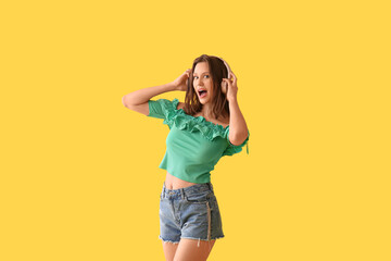 Beautiful young woman in modern headphones dancing on yellow background