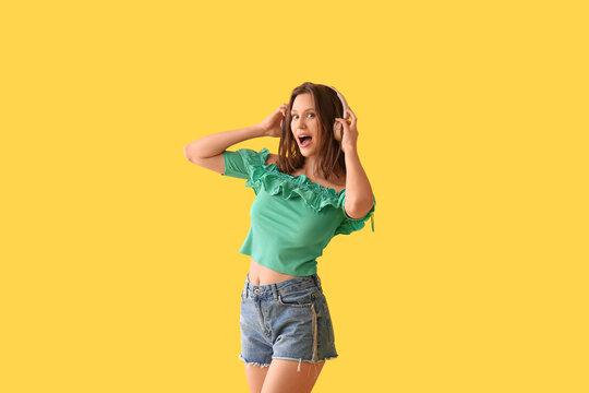 Fototapeta Beautiful young woman in modern headphones dancing on yellow background