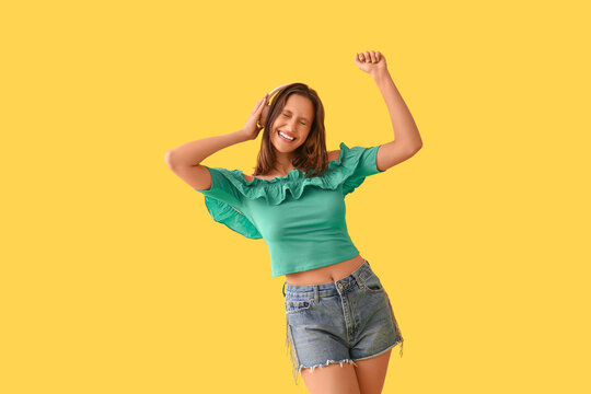 Fototapeta Beautiful young woman in modern headphones dancing on yellow background