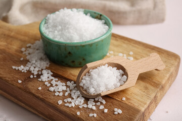 Wooden board with bowl and scoop of sea salt on light background