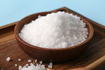 Wooden board with bowl of sea salt on color background, closeup