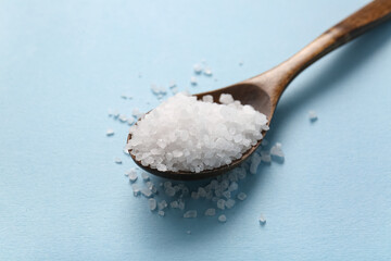Wooden spoon with sea salt on color background