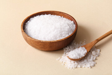 Wooden bowl and spoon with sea salt on color background