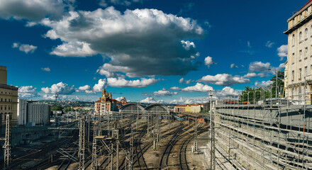Railway station with multiple train tracks under a dramatic sky filled with clouds and surrounded by urban architecture.