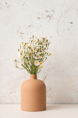 Vase with artificial chamomiles on table near white grunge wall