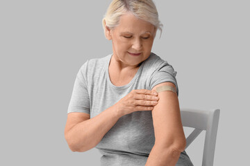 Senior woman with medical patch after vaccination sitting in chair on light background
