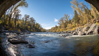 A vibrant river flows through a picturesque autumnal landscape, showcasing the interplay of water and rocky shores under a clear blue sky.
