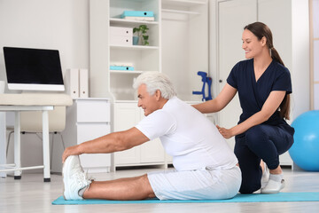 Obraz premium Female therapist with senior man training on mat in rehabilitation center