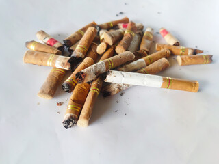 Close-up of a pile of used cigarette butts scattered on a white surface, symbolizing pollution, smoking addiction, health risks, and environmental waste caused by tobacco consumption.