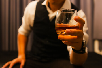 A highly experienced businessman in a tuxedo quietly pours whiskey in his home. A wealthy gentleman who exudes elegance, power and the contemplative luxury of nightlife.