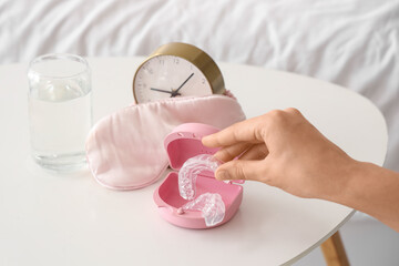 Female hand taking occlusal splint from table in bedroom, closeup