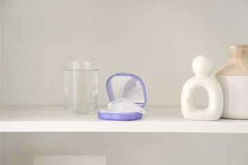 Box with occlusal splint and glass of water on shelf in room