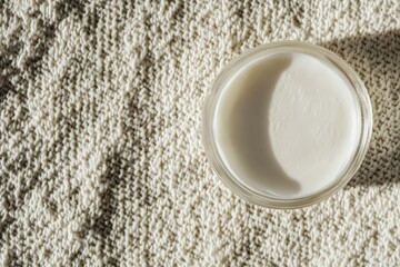 Top-down view of a cosmetic container on a textured fabric.