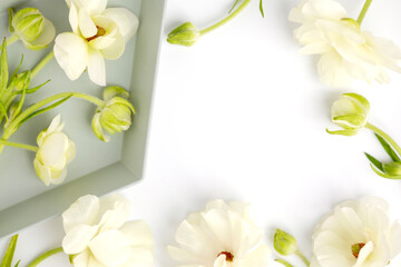 Flat lay composition of delicate white ranunculus flowers with green stems, artfully arranged with a tray on a bright white background. Copy space or product placement