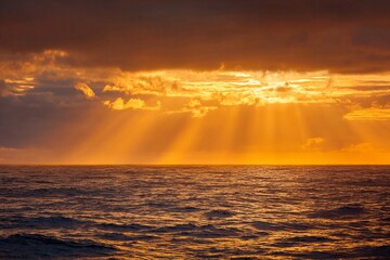 Golden sunset rays shining through dramatic clouds over ocean horizon