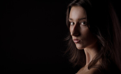 Naklejka premium Fashion model posing in studio with serious expression, looking over her shoulder against a dark background