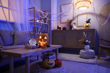 Interior of dark living room decorated for Halloween with sofa, table and glowing lamp