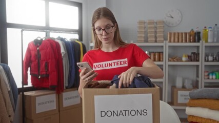 Woman volunteer sorts donations and taps smartphone in a donation center building; charity community.
