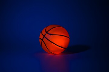 Fototapeta premium A vibrant basketball illuminated against a dark blue backdrop casting a subtle shadow on the surface