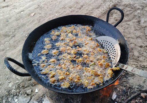 Crispy pakoras (fritters) being fried in a traditional pan. Freshly made and golden-brown, these tasty snacks are perfect for tea time or special occasions. This is a popular street food in India