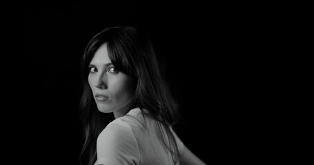 Black and white portrait of a young female model looking over her shoulder during a studio photoshoot, with a black background