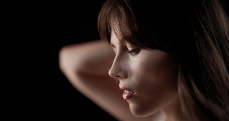 Profile of beautiful fashion model holding her hands behind her head during studio photoshoot,...