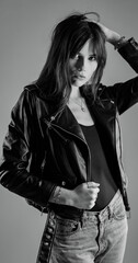 Black and white portrait of young woman with long hair wearing leather jacket and jeans, posing in studio