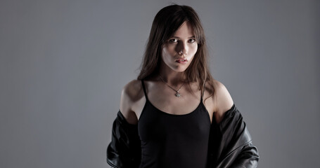 Young woman with long brown hair posing in studio wearing black clothes and leather jacket