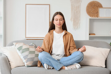 Young woman meditating on sofa at home. Zen concept