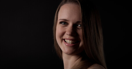 Fototapeta premium Studio portrait of beautiful young smiling model with long brown hair posing on black background