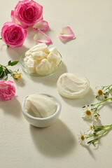 Close arrangement of shea butter with delicate roses and chamomile flowers. Beige soft background creates a clean scene for natural skincare advertising.