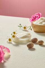 Close up of shea butter, pink roses and chamomile scattered across beige and pink background. Minimal skincare ingredient still life photo with blank space