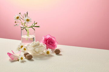 Soft beige background still life of shea butter, roses and chamomile flowers. Clean natural beauty ingredient arrangement with space for advertising layout. Blank space for design