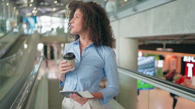 Latino woman drinking coffee while walking through airport terminal. 