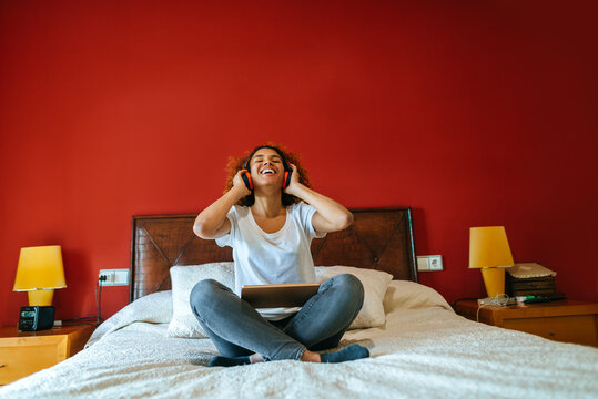 Happy woman listening to music with tablet sitting on the bed