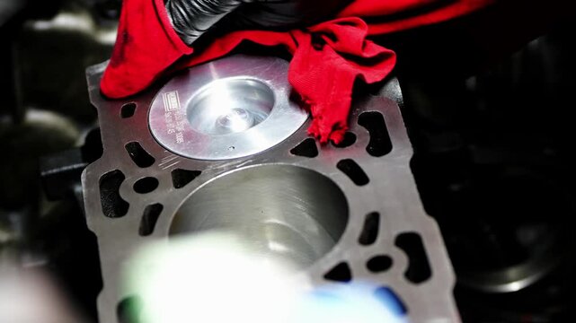 Detail video of mechanic hands cleaning car engine cylinder block with red cloth, wiping edges, channels, and shiny new pistons.