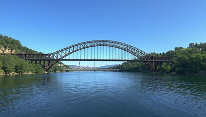 Naklejka premium A majestic steel arch bridge spans a wide river under clear skies