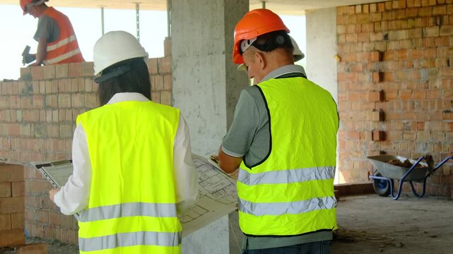 Project managers and worker look at layout studying features. Engineers and builder examine blueprint with room layouts discussing key points