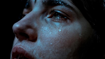 A person's face partially obscured by shadow, with a single tear. Regret, guilt, criminal, consequences, legal.