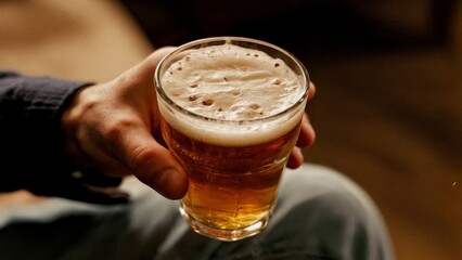 A person's hand holding a pint of beer with foam on top. Beer, pub, casual, fun, friends
